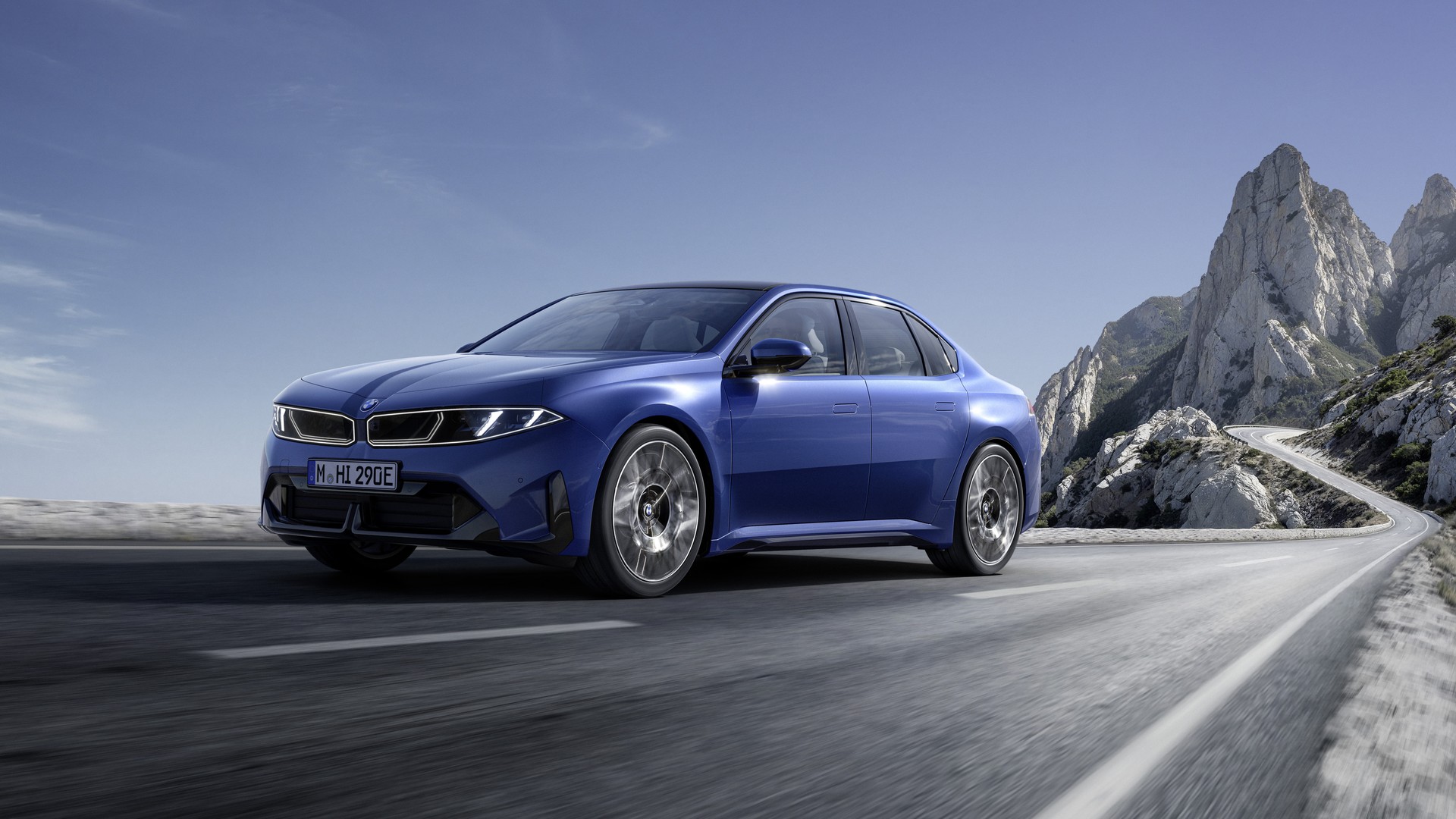 Blue 2027 BMW i3 50 xDrive sedan cornering on a coastal mountain road, front three-quarter view.