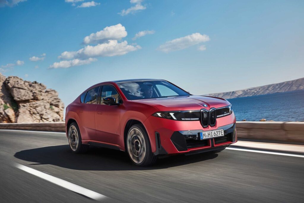 Red BMW iX4 driving on a coastal road, front three-quarter view