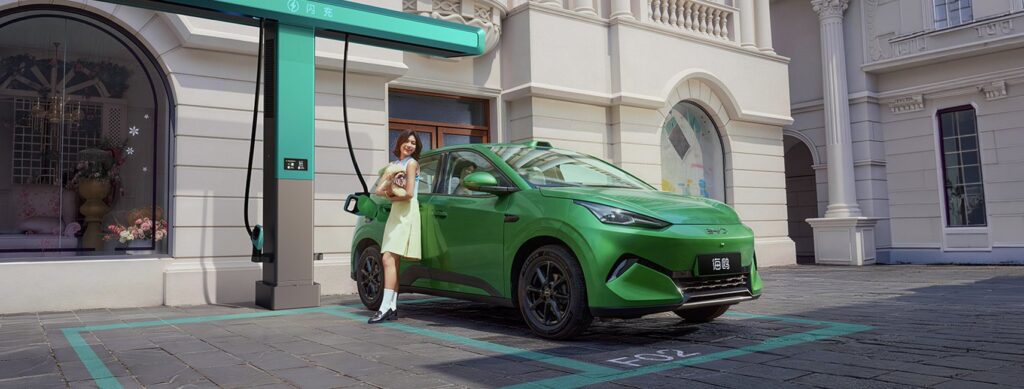 Green second-generation BYD Seagull plugged into a BYD Flash Charging post on a cobbled street