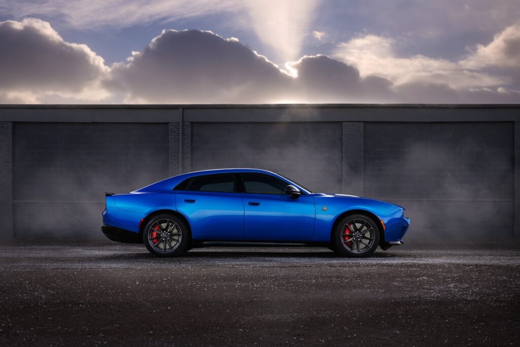 Blue 2027 Dodge Charger Daytona Scat Pack four-door in Bludicrous paint, side profile in front of a concrete wall