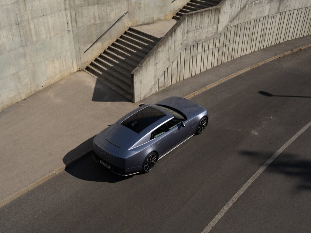 Jaguar Type 01 electric grand tourer in blue grey driving past a concrete wall and staircase