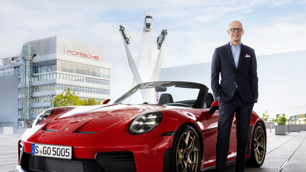 Porsche CEO Michael Leiters standing beside a red Porsche 911 convertible