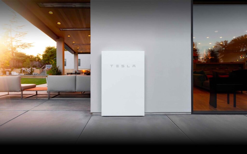 White Tesla Powerwall 3 home battery mounted on an exterior wall beside a patio