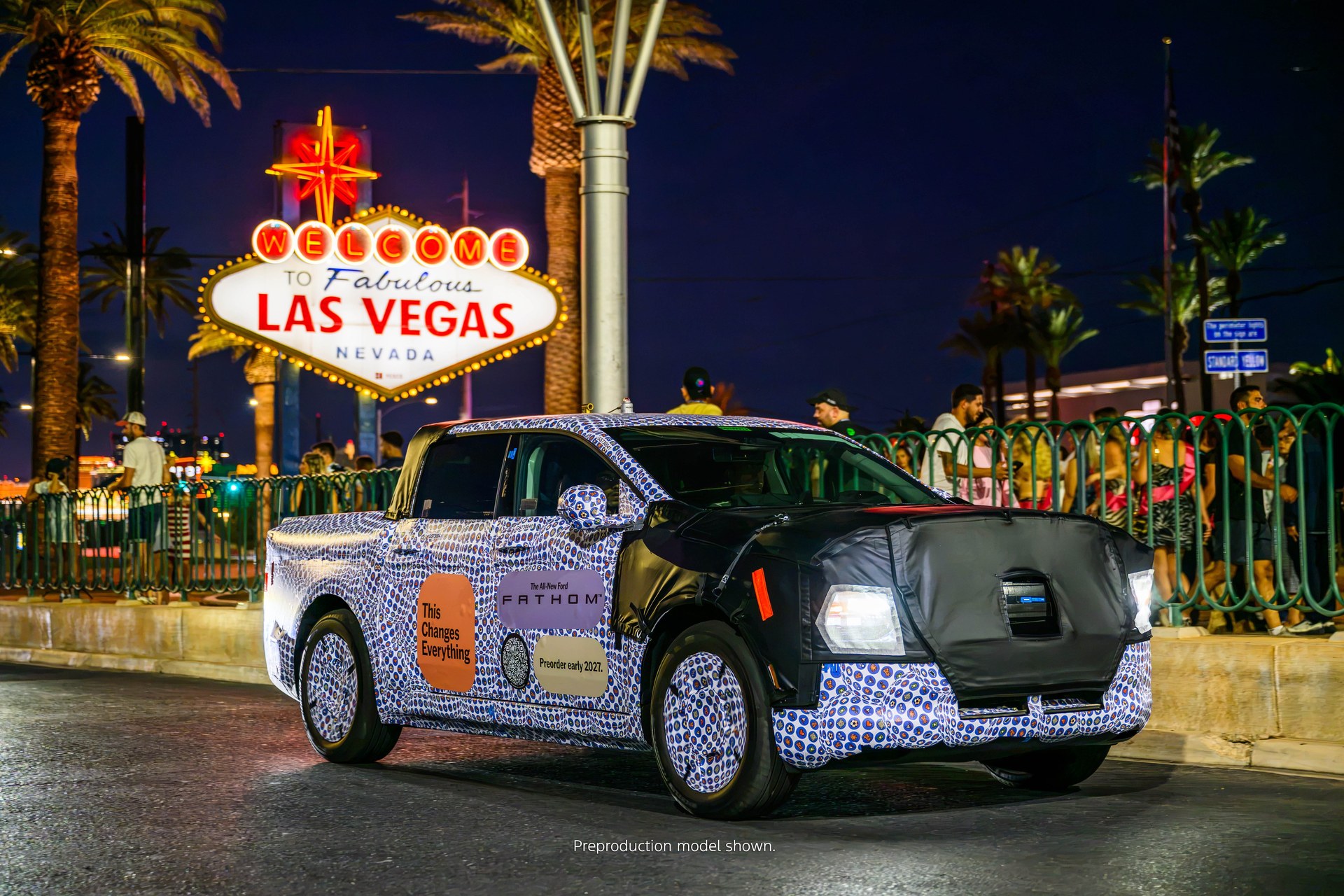 Camouflaged preproduction Ford Fathom electric pickup in front of the Welcome to Las Vegas sign at night