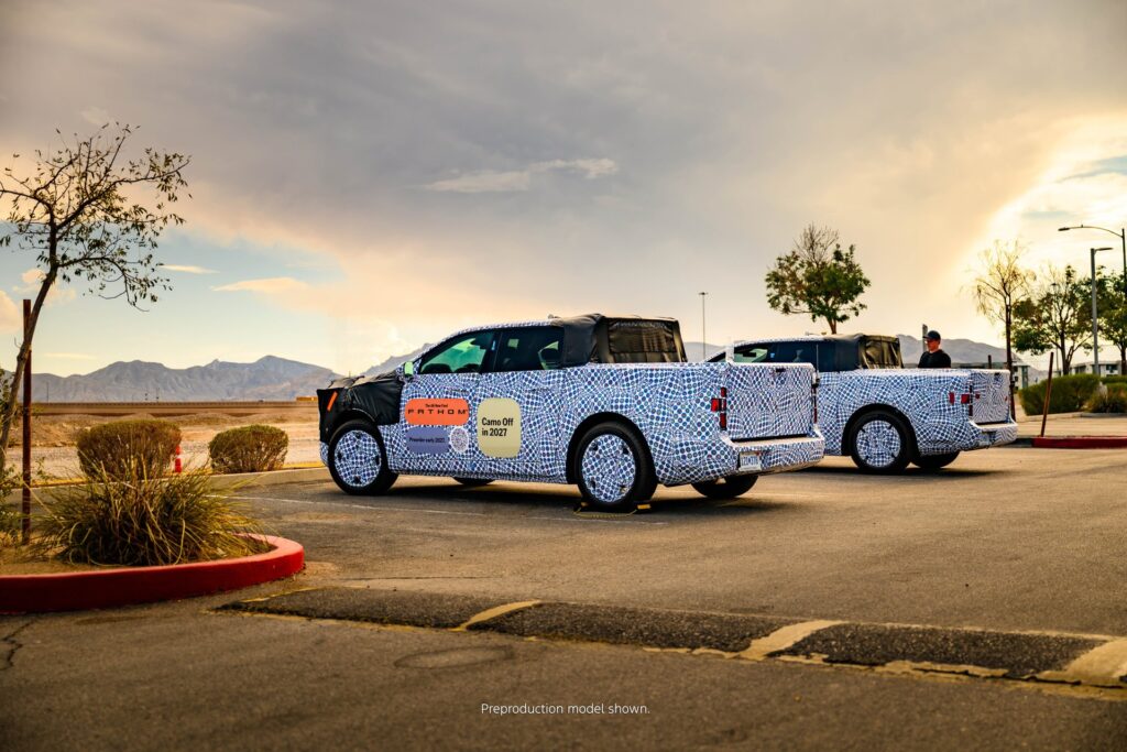 Two camouflaged preproduction Ford Fathom electric pickups seen from the rear three-quarter in the desert