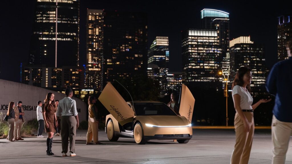 Gold Tesla Cybercab with both butterfly doors open as people gather on a plaza at night with the Austin skyline behind