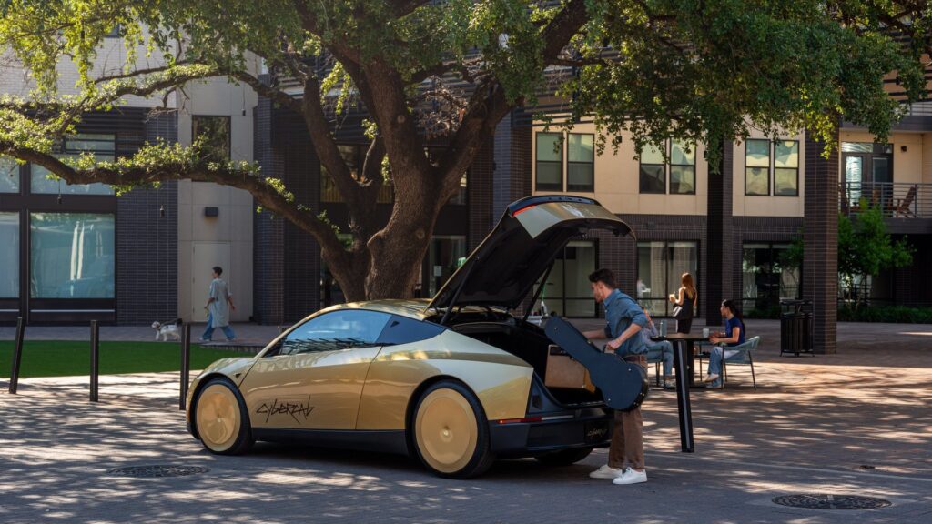 Gold Tesla Cybercab parked on a courtyard street with its rear hatch open as a rider loads a bag