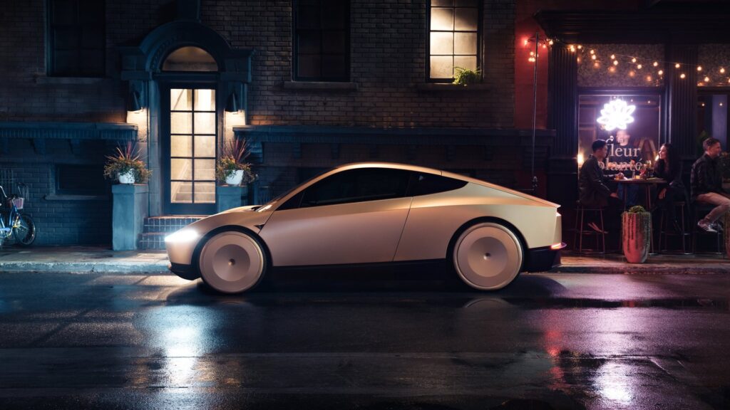 Gold Tesla Cybercab in profile on a rain-slicked street at night beside a lit cafe