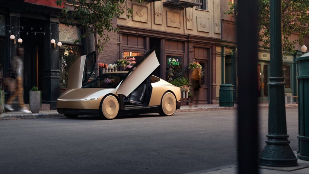 Gold Tesla Cybercab with both butterfly doors open on a street lined with old storefronts