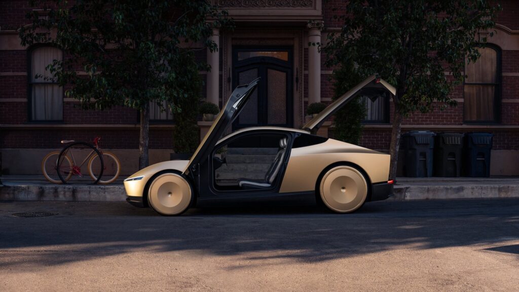 Side view of a gold Tesla Cybercab with both doors raised in front of a brick townhouse at sunset
