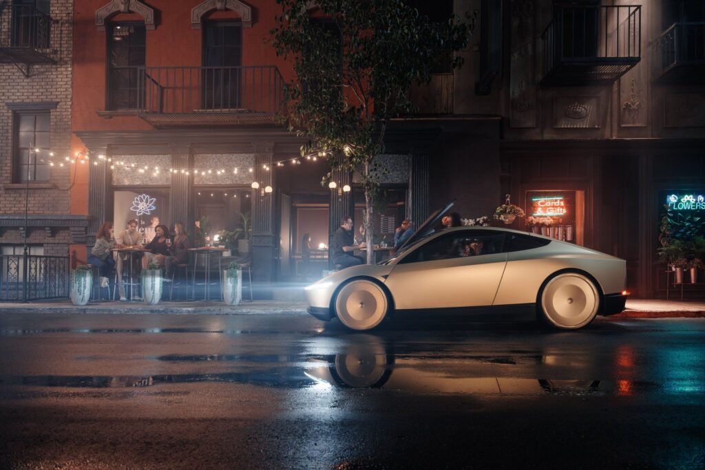 Gold Tesla Cybercab on a reflective wet street at night beside a crowded outdoor cafe