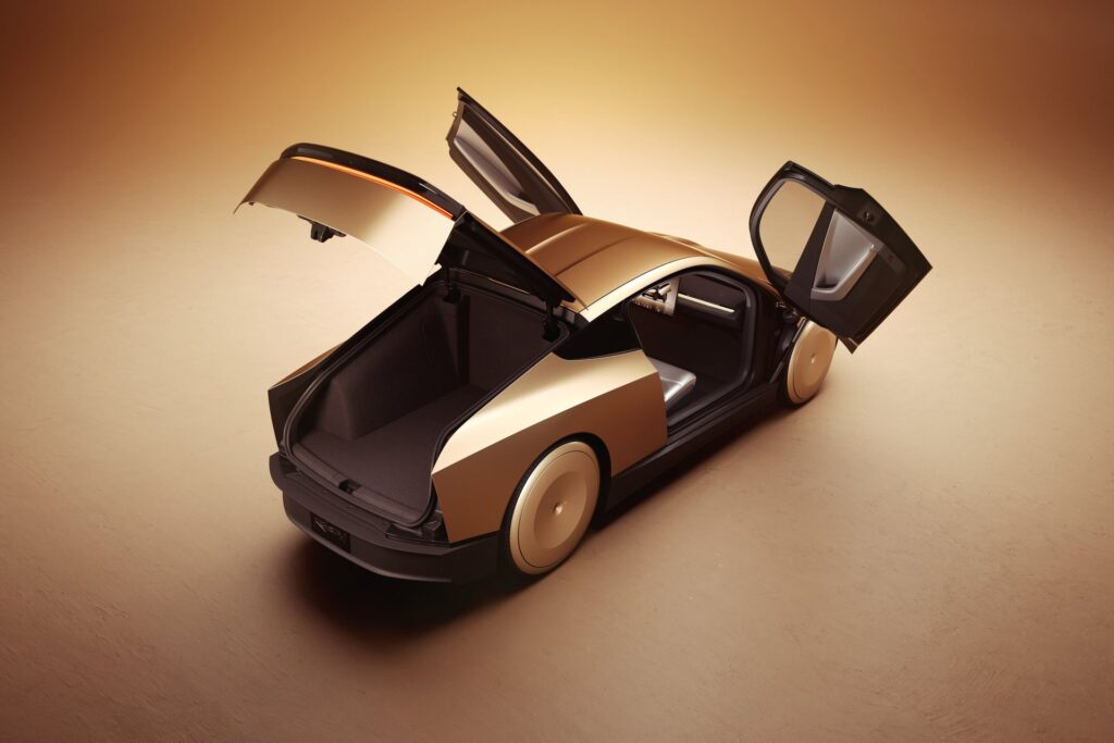 Overhead rear view of a gold Tesla Cybercab with both doors and the rear hatch open showing the cargo area