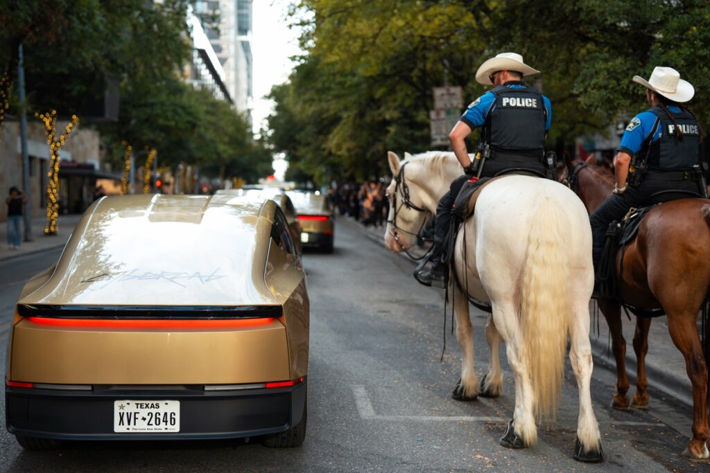 Gold Tesla Cybercab seen from the rear on a downtown Austin street next to mounted police officers