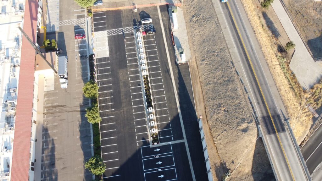 Overhead view of a Tesla Supercharger lot with a long row of stalls next to a highway