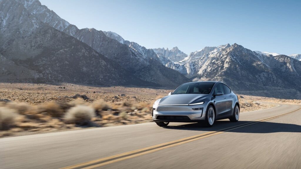 Silver Tesla Model Y driving on a desert road with snow-capped mountains behind it