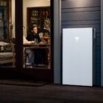 Tesla Powerwall 3 mounted outside a lit home at night