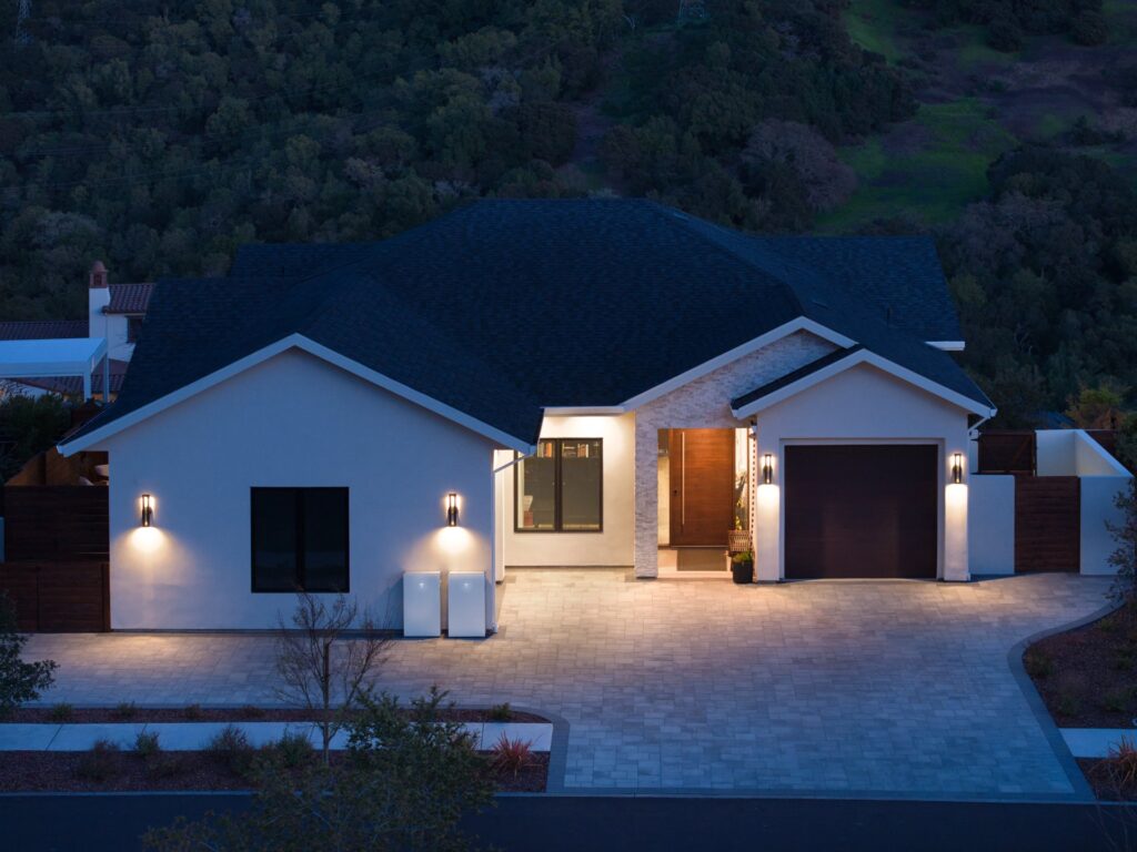 Two Tesla Powerwall units mounted outside a home at dusk with the lights on