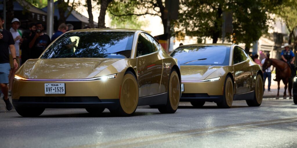 Two gold Tesla Cybercabs driving past a crowd on an Austin street