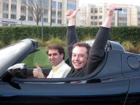 Elon Musk raises his arms in an original Tesla Roadster around the first delivery in 2008