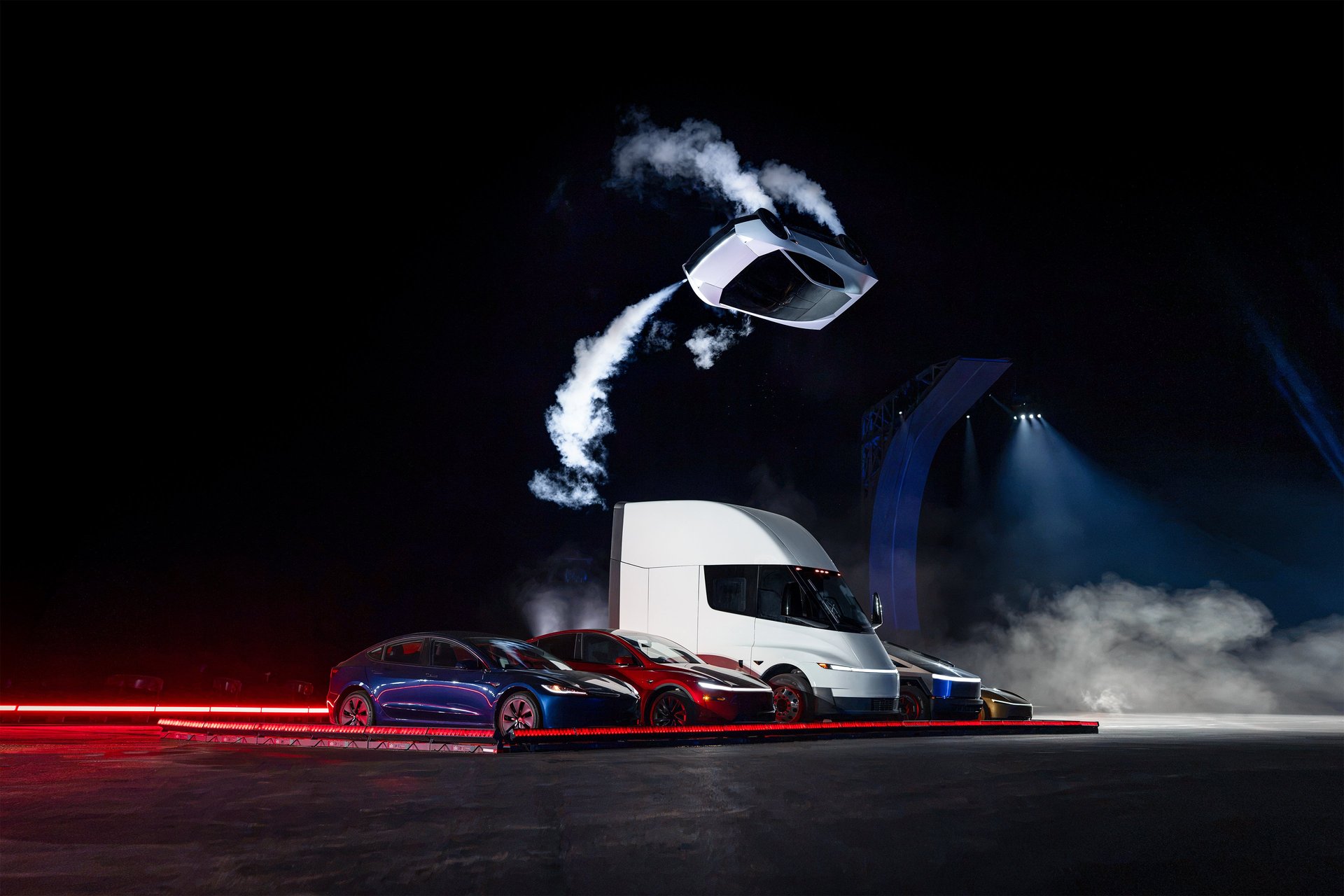 Tesla Roadster flying over a lineup of Tesla vehicles including the Semi, trailing thruster smoke at the reveal