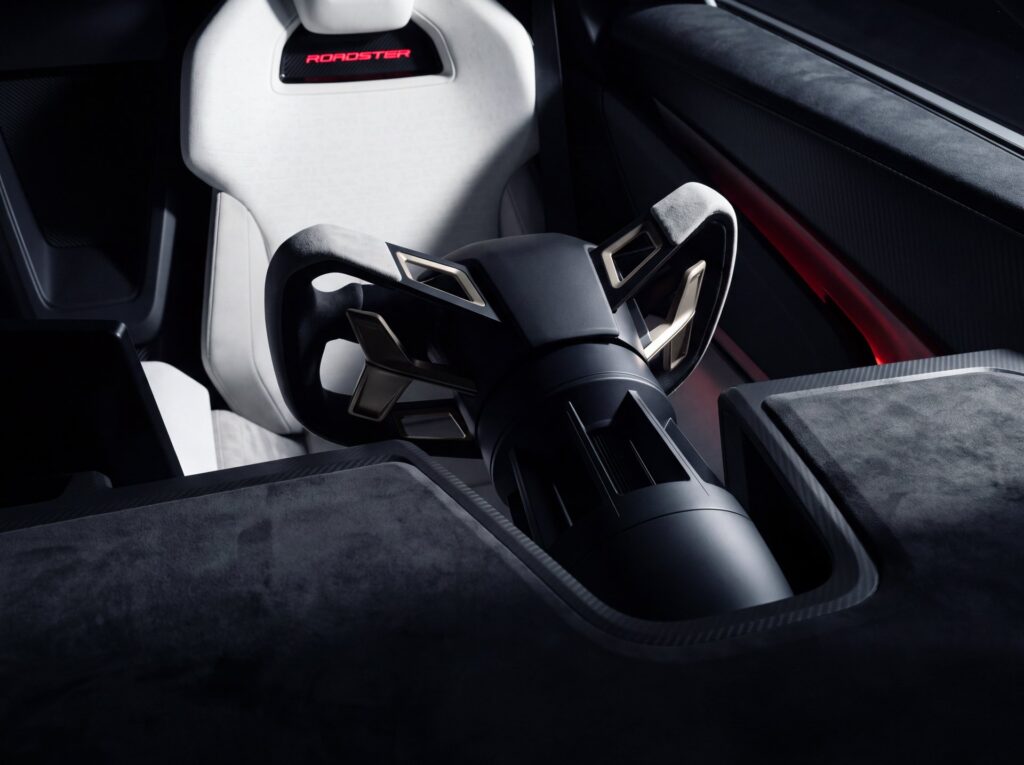 Tesla Roadster yoke steering wheel and column in front of a white seat with a red ROADSTER logo