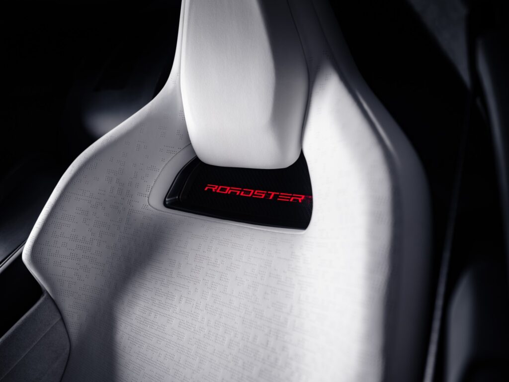 Close-up of a white Tesla Roadster sport seat with a red ROADSTER logo below the headrest