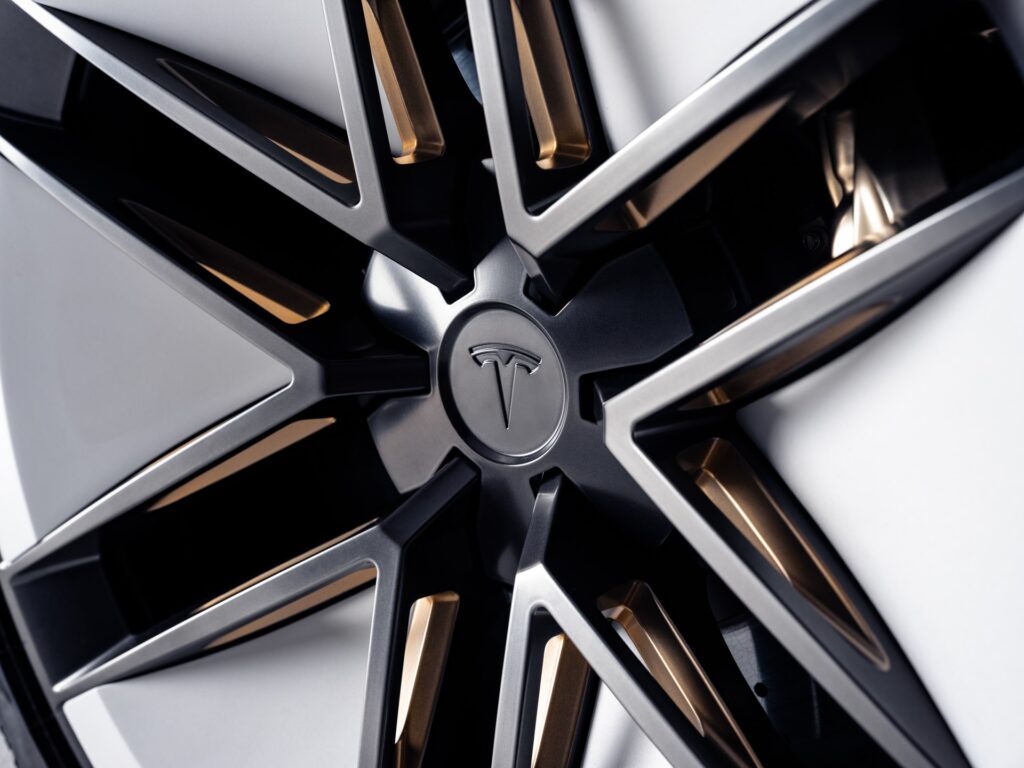 Close-up of a white Tesla Roadster wheel with sharp angular spokes and a Tesla logo center cap