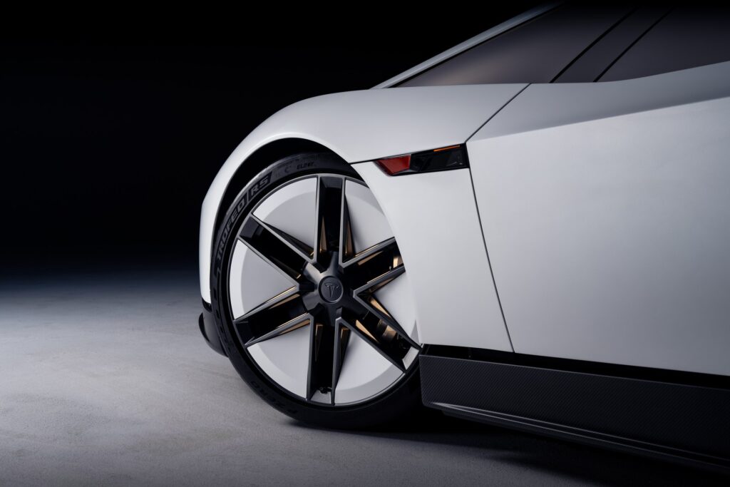 Front wheel and faceted white bodywork of the Tesla Roadster against a dark backdrop