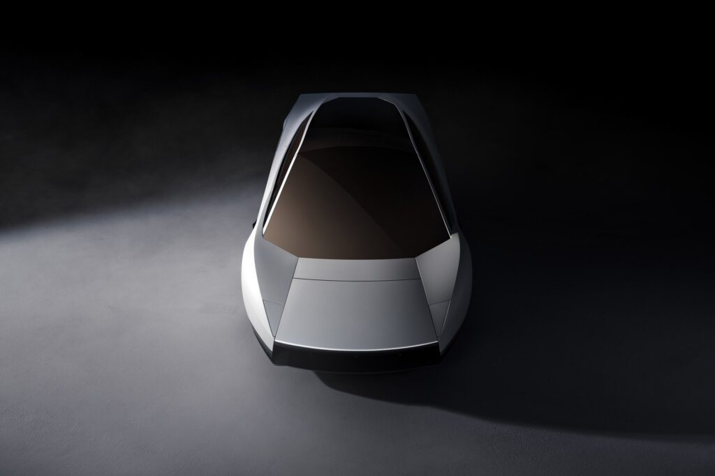 Overhead front view of a white Tesla Roadster with a tinted glass roof under a spotlight