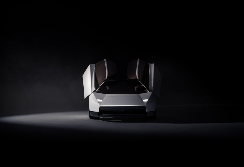 Front view of a white Tesla Roadster under a spotlight with both doors raised