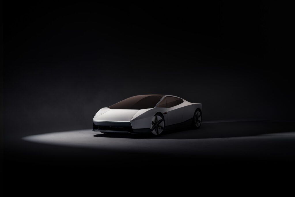 Front three-quarter view of a white Tesla Roadster under a spotlight on a dark stage