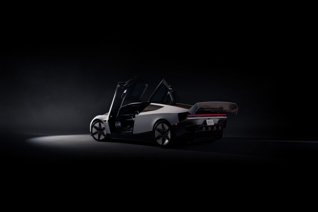 Rear three-quarter view of a white Tesla Roadster with its doors raised and wing deployed