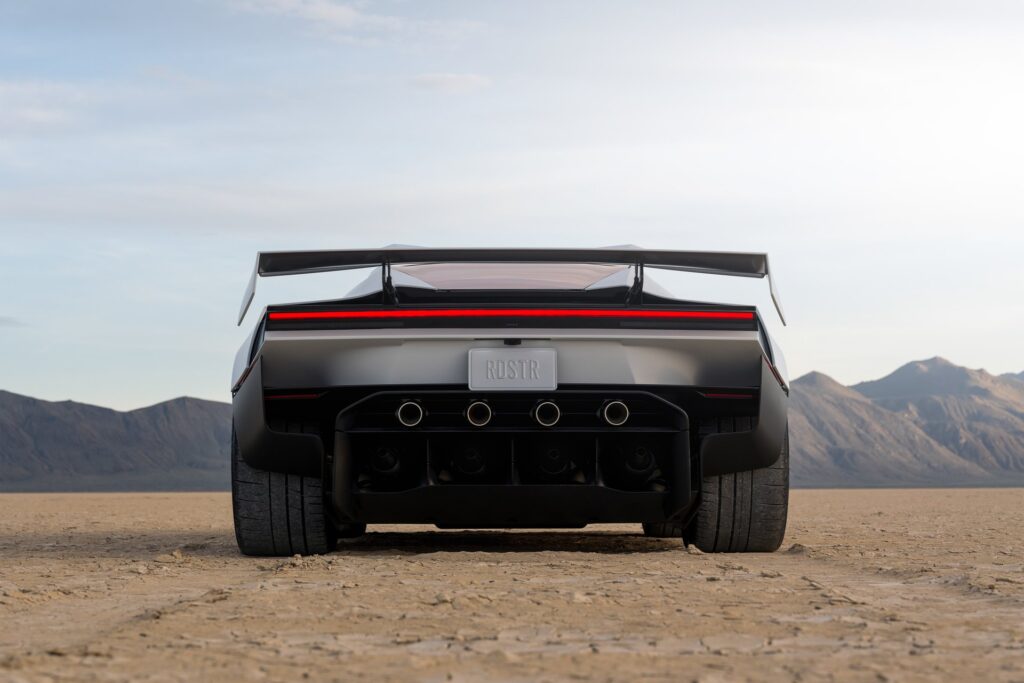 Rear view of the Tesla Roadster on a desert lakebed with its large wing raised and four thruster nozzles