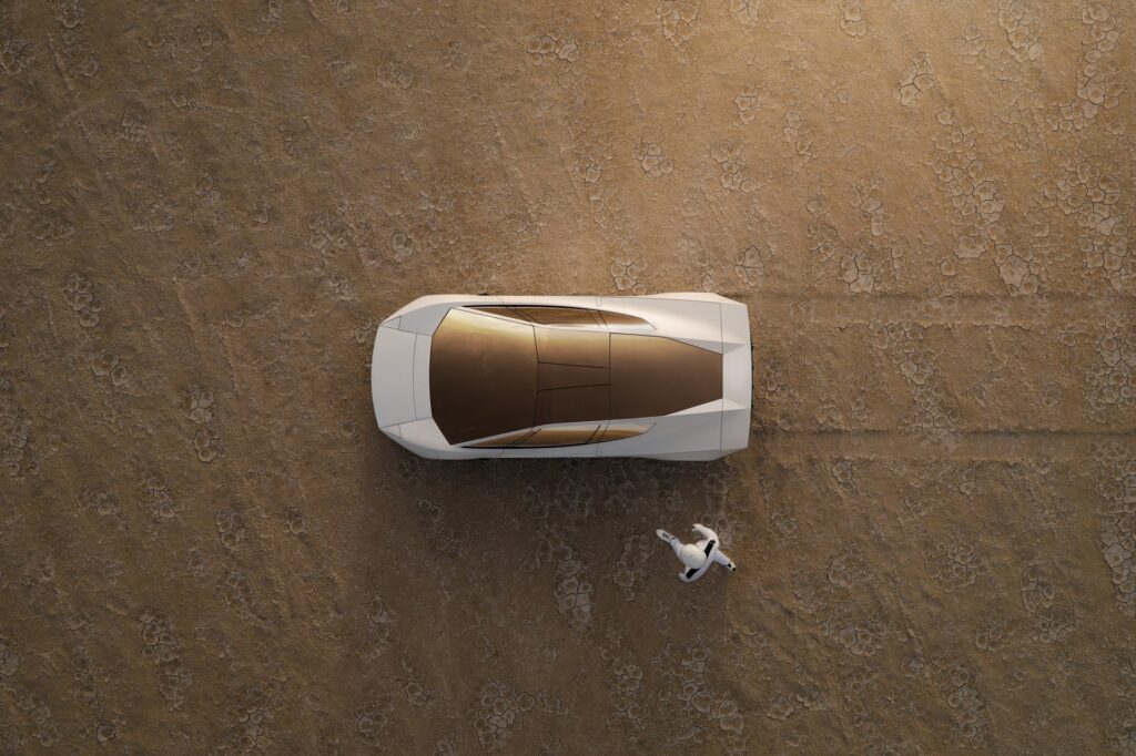 Aerial view of a white Tesla Roadster on a dry lakebed with a driver in a white suit lying beside it