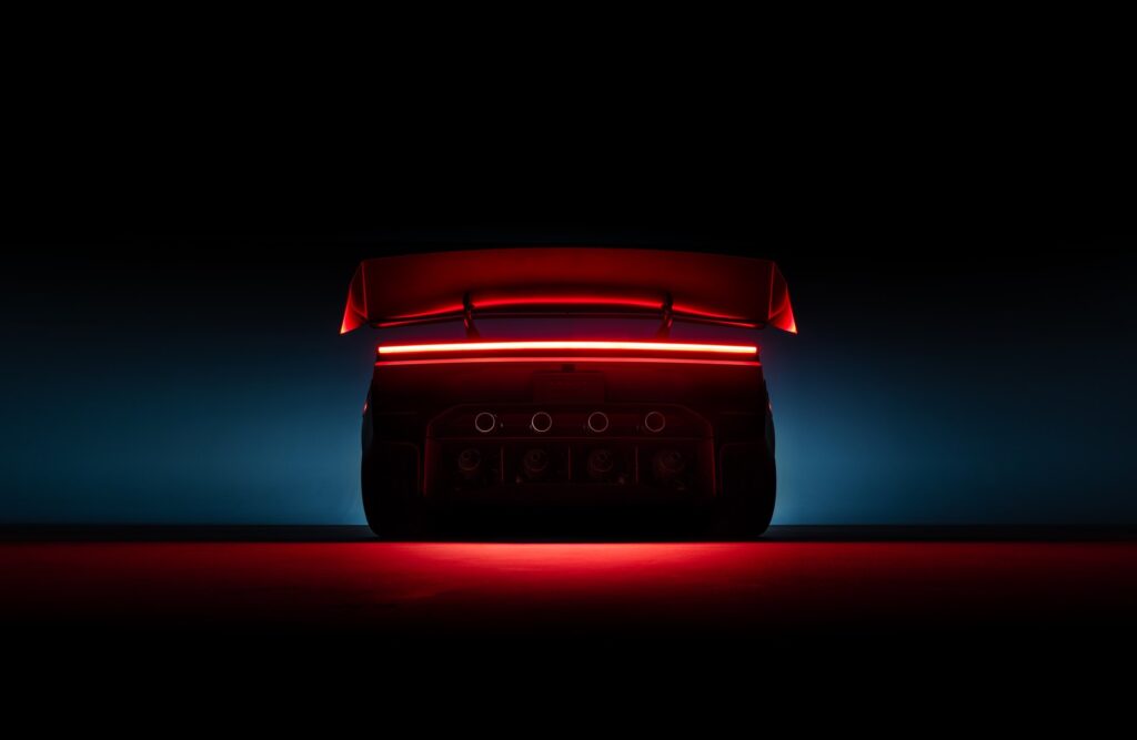 Tesla Roadster rear at night with its red light bar and wing glowing against a blue haze