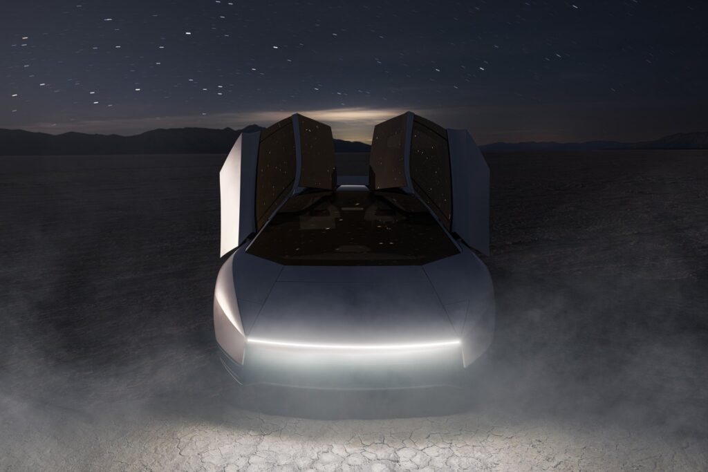 Front of a Tesla Roadster at night on a lakebed with both doors raised and a white light bar lit