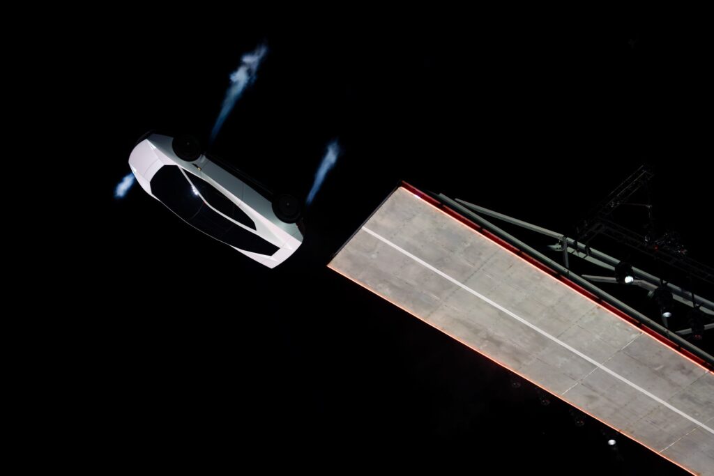 White Tesla Roadster upside down as it leaves the top of the ramp with blue thrusters firing