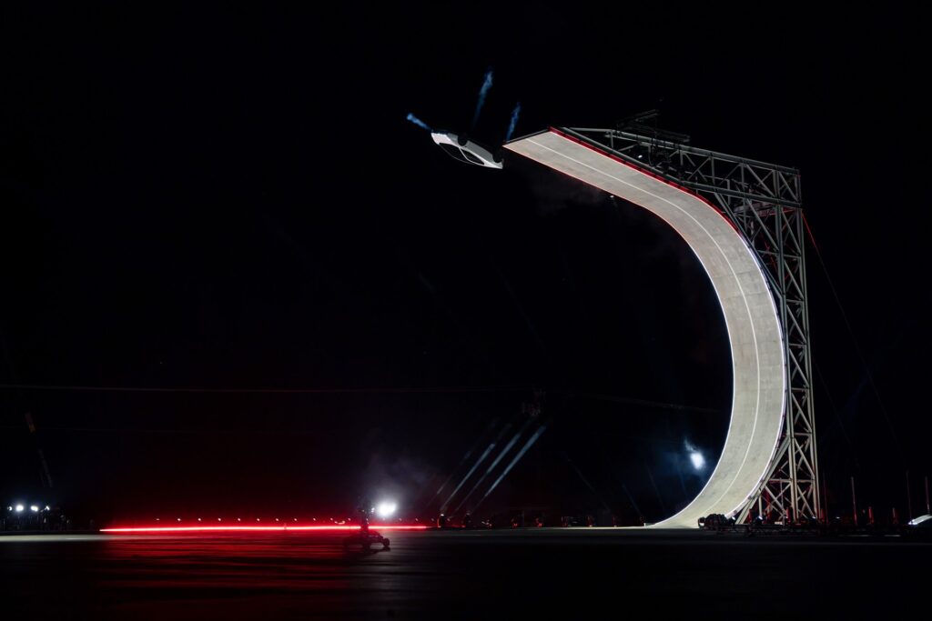 Tesla Roadster launching off the top of the C-shaped ramp at night with thrusters firing