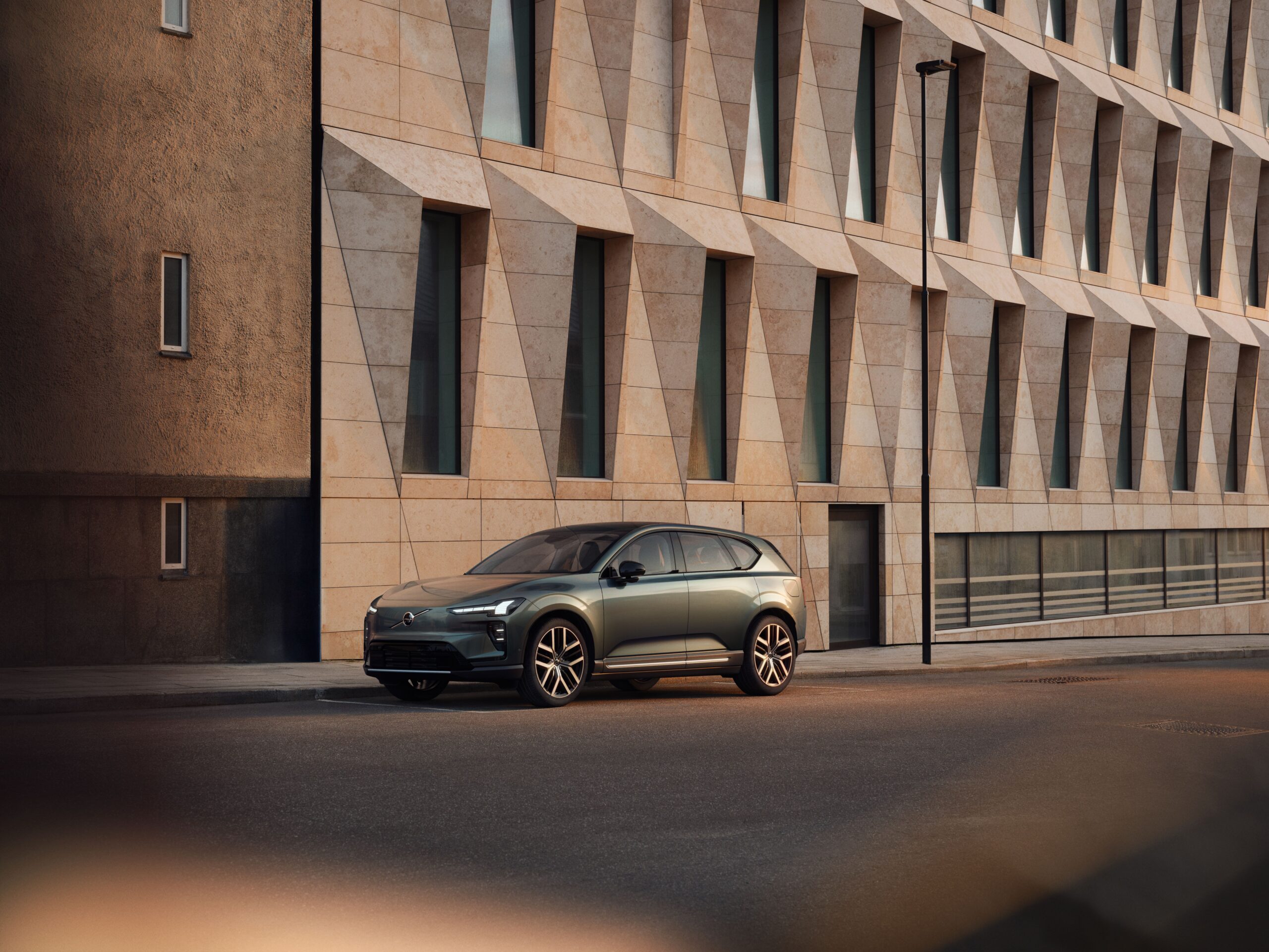 Grey Volvo EX60 electric SUV parked beside a stone building